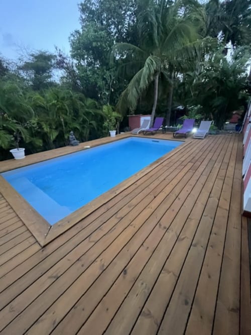 Terrasse en bois avec piscine rectangulaire bleue entourée de végétation tropicale aux Villas rouges, Saint-François