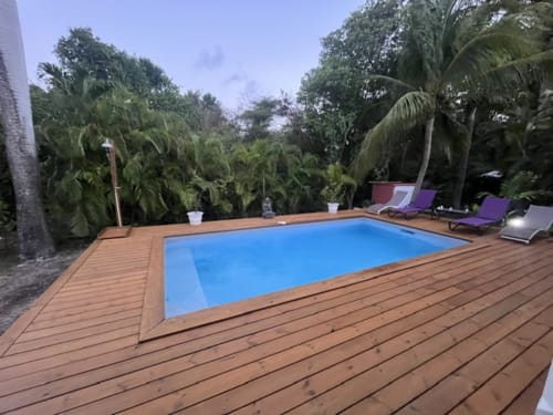 Piscine rectangulaire aux eaux turquoise, terrasse en bois, chaises longues et jardins tropicaux luxuriants aux Villas