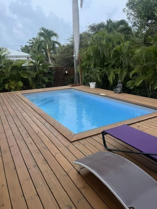 Piscine rectangulaire privée aux eaux turquoise sur terrasse en bois, entourée de palmiers tropicaux à la Villa la Désirade