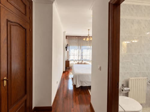 Pasillo con puertas y suelos de madera que conduce al dormitorio con cama blanca del apartamento Amieiro, Baiona