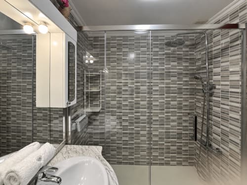 Cuarto de baño moderno con azulejos grises a rayas, ducha de cristal, lavamanos de mármol y espejo en el apartamento Holibai Amieiro