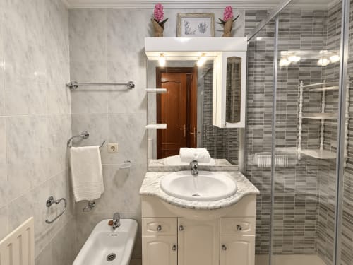 Cuarto de baño moderno en el apartamento Amieiro, Baiona con baldosas de mármol, lavabo circular, mampara de ducha y toallero calefactable
