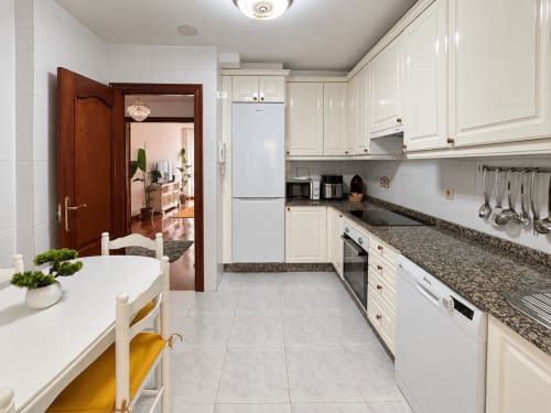 Cocina moderna con muebles blancos, encimeras de granito y electrodomésticos de acero inoxidable en el apartamento Amieiro, Baiona