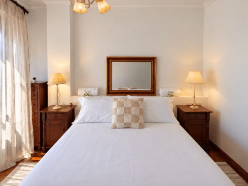 Dormitorio luminoso en el apartamento Amieiro, Baiona con cama blanca, mesillas de madera, lámparas y espejo