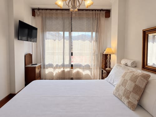 Habitación luminosa en apartamento Holibai Baiona con vistas a la ciudad, ropa de cama blanca, muebles de madera y puertas de vidrio que se abren a