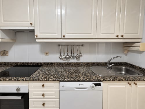 Cocina moderna del apartamento Holibai en Baiona con muebles blancos, encimera de granito y fregadero de acero inoxidable