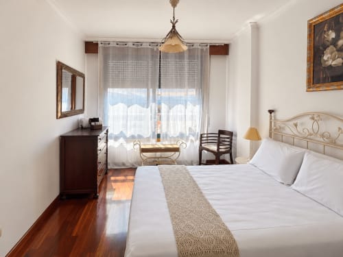Dormitorio luminoso del apartamento Amieiro en Baiona con cama de matrimonio, suelos de madera, vistas a la ciudad y decoración clásica