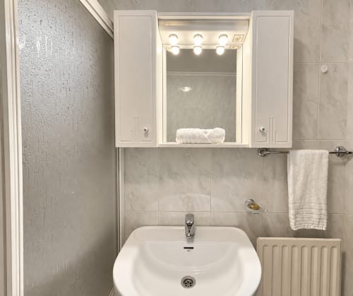 Baño moderno en apartamento de Baiona con lavamanos blanco, espejo iluminado y paredes con azulejos beige
