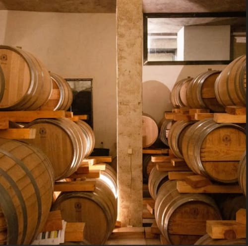Cellier de tonneaux vieillis à Domaine Lantana, un gîte français à Lecci avec des fûts de chêne empilés sur des supports en bois.