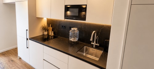 Cozinha moderna com armários brancos, bancada em mármore negro, pia em aço inoxidável e eletrodomésticos embutidos na House Park BnB