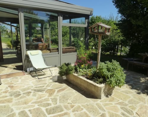 Terrasse ensoleillée avec transat, fleurs en pot et mangeoire pour oiseaux à La Ferme Buissonnière, Biol, France