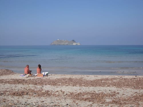 Clients se détendant sur la plage de galets de la villa Cap Corse, avec vue sur l'île et la mer Méditerranée turquoise