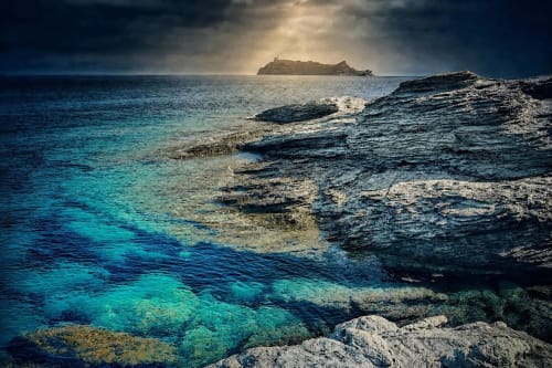 Eaux turquoise méditerranéennes et côte rocheuse près d'Ersa, Corse, avec île lointaine et ciel dramatique