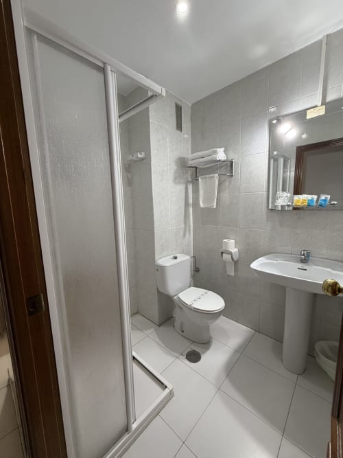 Baño moderno del Hotel JM El Emigrante en Villanueva de la Serena con ducha, inodoro, lavamanos y paredes con azulejos grises