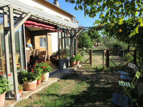 Véranda de La Ferme Buissonnière avec fleurs en pot et salon de jardin à Biol