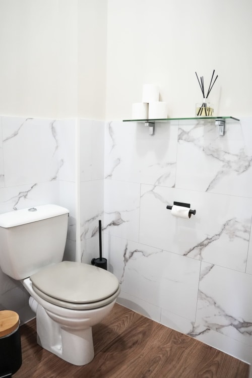 Baño moderno del hotel Le Saint Laurans en Aurignac con azulejos de mármol, inodoro blanco y estantería de cristal con artículos de aseo