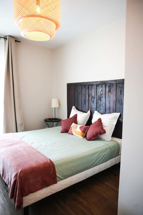 Dormitorio moderno en el hotel Le Saint Laurans en Aurignac con cabecero de madera oscura, almohadas burdeos y lámpara de techo tejida