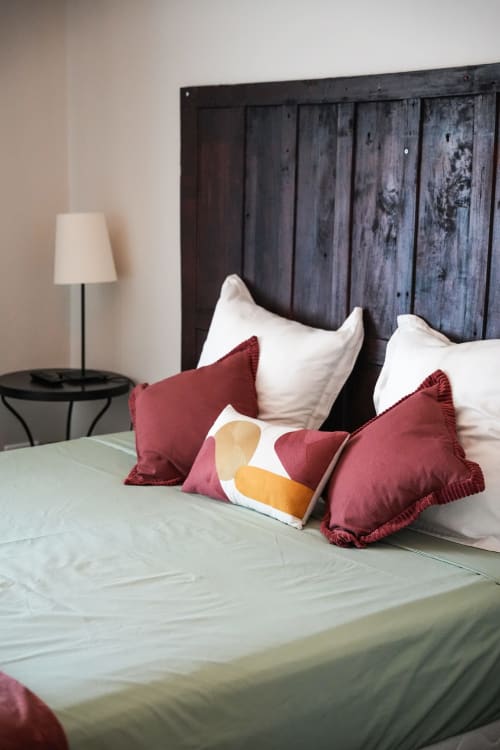 Cama con almohadas burdeos y blancas en el hotel Le Saint Laurans en Aurignac, con cabecero de madera oscura y lámpara de mesilla