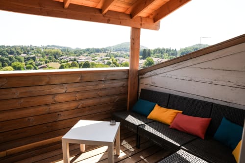 Terraza del hotel Le Saint Laurans en Aurignac con pérgola de madera, sofá de ratán negro, cojines coloridos y vistas al valle