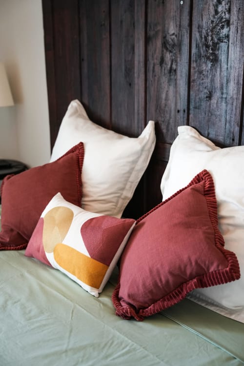 Cojines decorativos en la cama del hotel Le Saint Laurans en Aurignac, con cojines burdeos con patrones geométricos y
