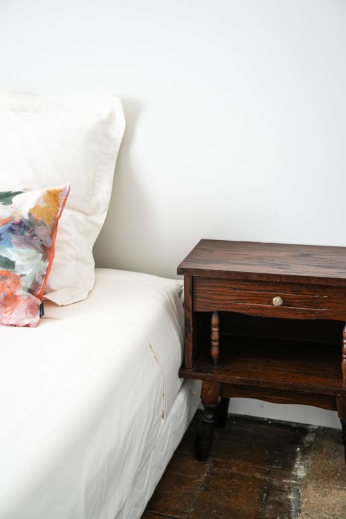 Cozy bedroom at Le Saint Laurans hotel in Aurignac with white bedding, colorful pillow, and wooden nightstand
