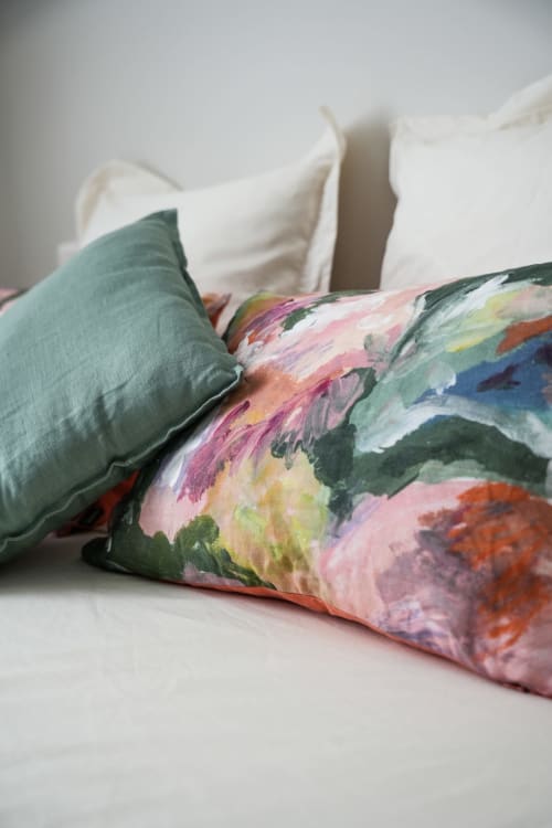 Colorful floral pillow and sage green cushion on white bedding at Le Saint Laurans hotel in Aurignac