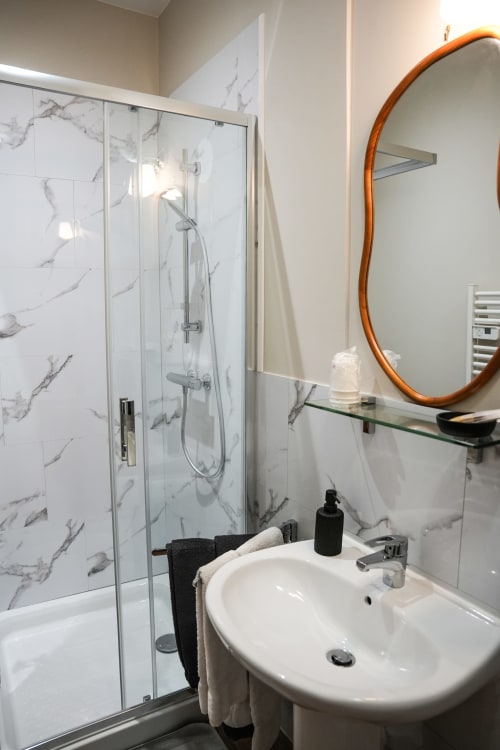 Baño moderno del hotel Le Saint Laurans en Aurignac con ducha de mármol, espejo redondo naranja y lavabo blanco