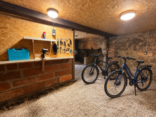 Salle de rangement des vélos à l'hôtel Locacharme à Blois avec vélos, tableau d'outils et éclairage lumineux