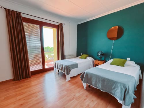 Bright family room at Balcó del Priorat in Tarragona with two beds, teal accent wall, wooden floors, and mountain view