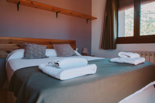 Balcó del Priorat family room with white towels on bed, mountain views through windows, wooden headboard and shelving in