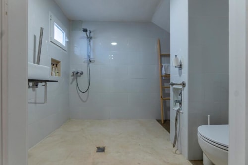 Ducha a ras de suelo moderna con azulejos blancos, alcachofa de lluvia y estanterías de madera en el baño de la habitación triple Cal Xot, Poble Nou