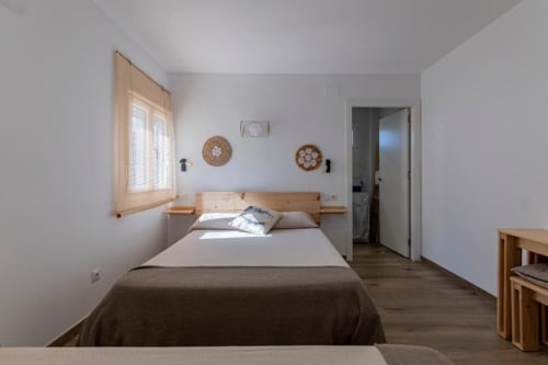Amplia habitación luminosa en el Cal Xot B&B de Poble Nou del Delta con cama de madera, decoración mural tejida y vistas al patio interior