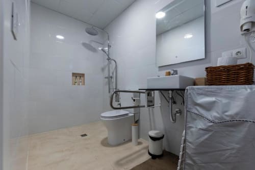 Baño accesible para sillas de ruedas en Cal Xot con ducha sin barreras, inodoro, lavabo y barras de seguridad