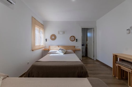 Habitación cuádruple luminosa en Cal Xot B&B con cama de madera, decoración tejida en la pared y luz natural desde ventana hacia el interior