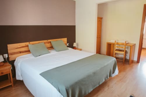 Spacious double bedroom at Balcó del Priorat hotel in Tarragona with wooden furniture, white linens, and sage green accents.