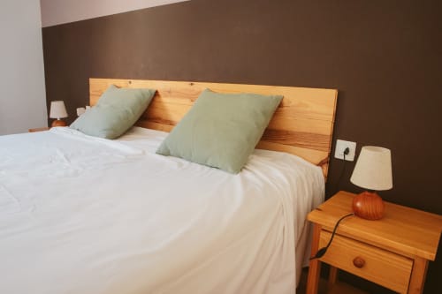 Balcó del Priorat hotel room with wooden bed headboard, white linens, green pillows, and wooden nightstand with lamp in