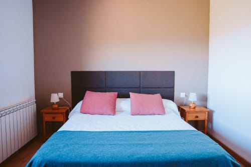 Moderno dormitorio doble en Balcó del Priorat, Tarragona, con manta azul, almohadas rosa y mesillas de madera