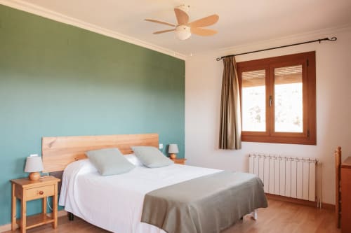 Spacious corner bedroom at Balcó del Priorat, Tarragona, with turquoise accent wall, wooden bed, and mountain views