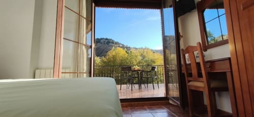 Habitación del hostal Monachil con puertas de terraza abiertas con vistas a las montañas, amueblada con mesa y sillas