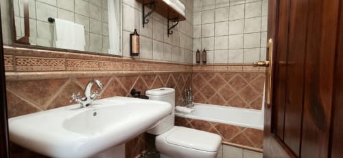 Baño elegante en la Hospedería Puerta a los Cahorros de Monachil con lavamanos, inodoro, bañera y paredes alicatadas
