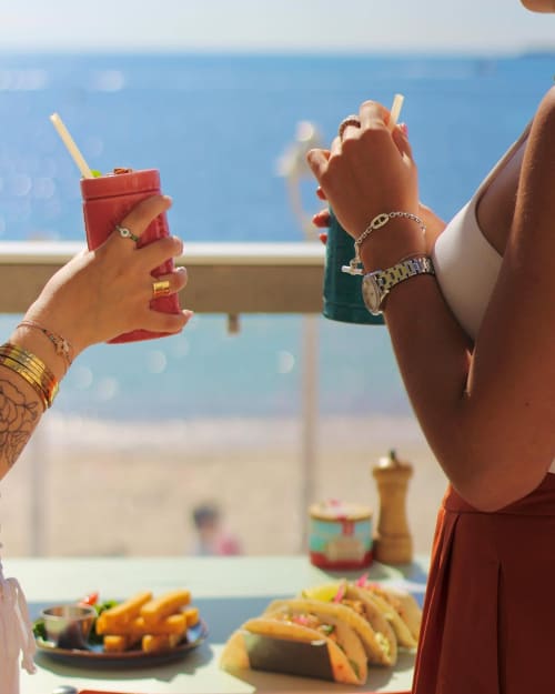 Deux femmes savourant des cocktails et des tacos sur la terrasse d'un hôtel de Cannes avec vue sur la mer
