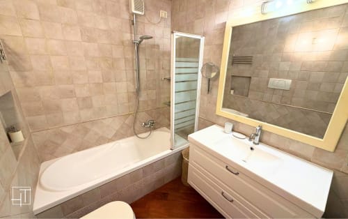 Bathroom in Padova apartment with bathtub, white vanity, mirror, and beige tile walls