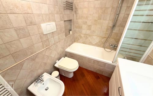 Modern bathroom with beige tiles, white toilet and bidet, wooden floor, and shower enclosure in Padova apartment