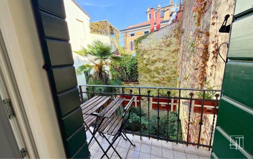 Sunny balcony terrace with wooden chairs overlooking historic Padova courtyard, ivy-covered walls, and colorful buildings in
