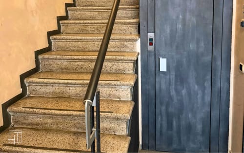 Stone staircase with brass handrail and dark elevator doors in Padova apartment building