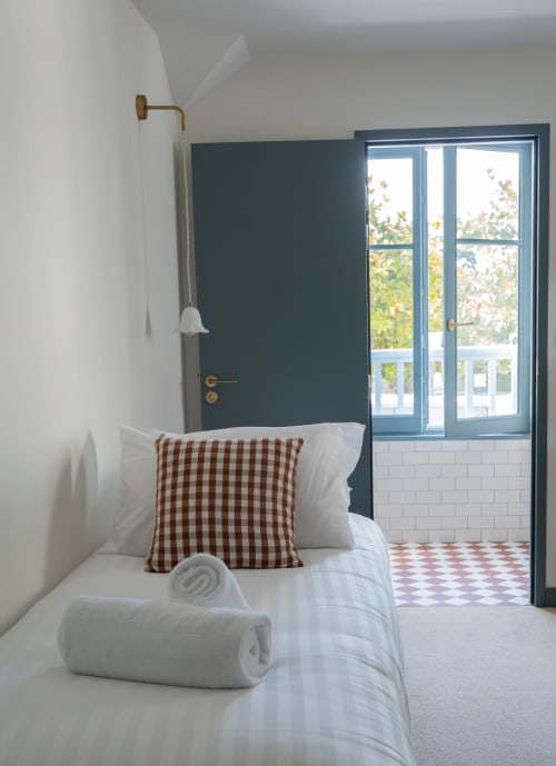 Chambre d'hôtel Saint Enogat avec lit, oreiller à carreaux marron, serviettes blanches et portes vitrées ouvrant sur balcon