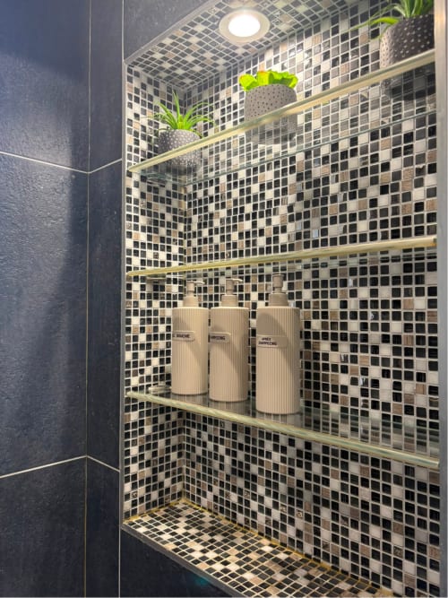 Niche de douche contemporaine avec carrelage mosaïque noir, étagères en laiton, produits de toilette et plantes en pot à l'appartement Le Paradis Des Logis