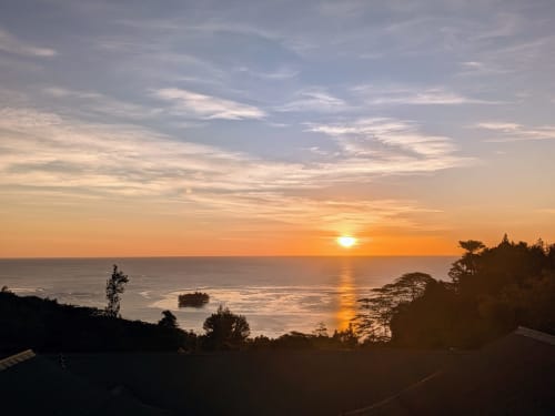 Vue du coucher de soleil sur l'océan depuis Fare Tihi Moana à Tumaraa, arbres en silhouette et ciel doré