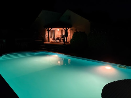 Illuminated pool at night with cottage and lit patio in background at L'Instant Sauvage, Dun les Places