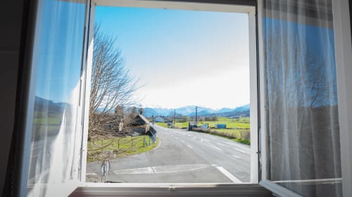 Vista pela janela aberta da zona rural francesa com montanhas, campos e estrada da Chambre Cocoon em Maison de Barlest